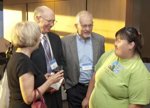 This is an image showing Bob Glover, his wife Toni Falbo and daughter Rachel, and Bob McPherson.  They are in business and casual attire and are all engaged in conversation.