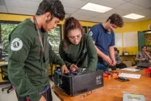 This image shows students in a classroom working on an electronic item.