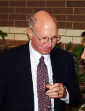 This is an image of Bob Glover, PhD.  He is light skinned with gray hair.  He is waeing thin-rimmed glasses and a dark suit with a white shirt and geometric-patterend tie.