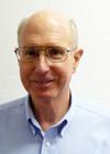 This is an image of a smiling Bob Glover, PhD.  He has light skin and gray hair.  He is wearing thin-framed glasses and a blue button-down shirt.