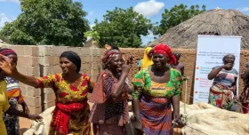 This is the report cover for Nuru Nigeria 2023 Endline Impact Report.  It shows Nigerian women laughing and smiling while walking with cows in front of a wall in a village.