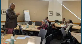 This is a picture of a presentation at the Opportunity Youth Forum.  It shows a man standing at the front of the room with people seated at several tablesin a classroom-style setting. 