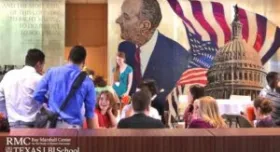This is a picture of the Lyndon B Johnson mural at the LBJ School of Public Affairs.  There are graduate students sitting and standing during an event.