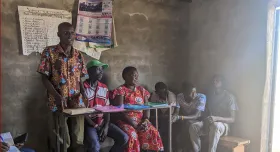 This is the report cover for Nuru Kenya 2024 Baringo County Baseline.  It shows people sitting and standing inside a building in Kenya.